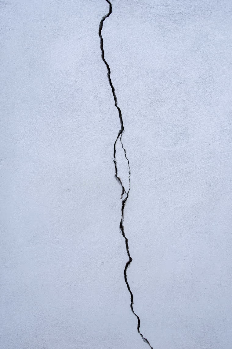 A crack running the height of a white stucco wall, varying in width and stepping sideways partway down its length